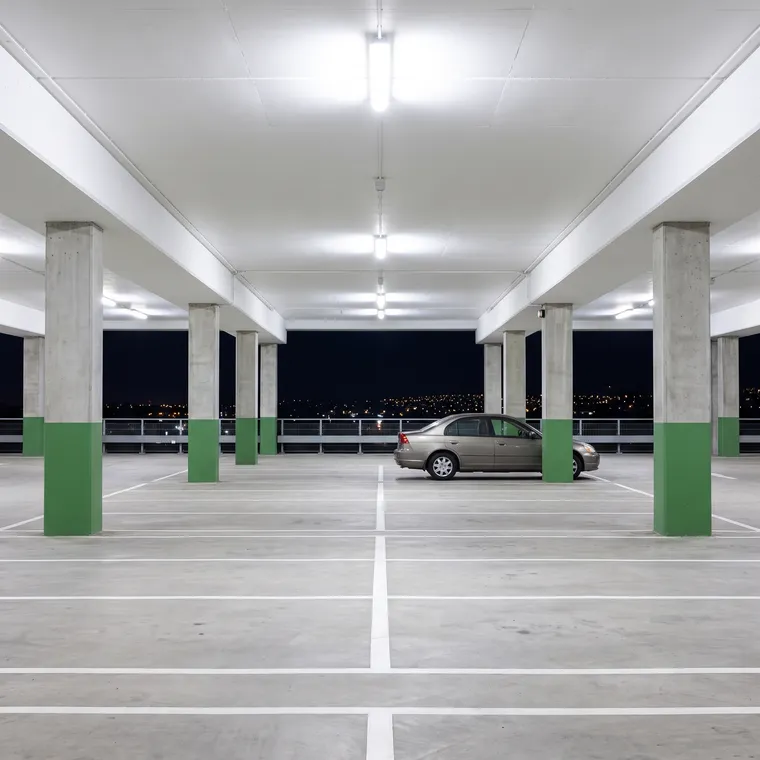 Generated scene: an empty covered parking level at night with green-painted column bases, white floor lines and distant city lights.